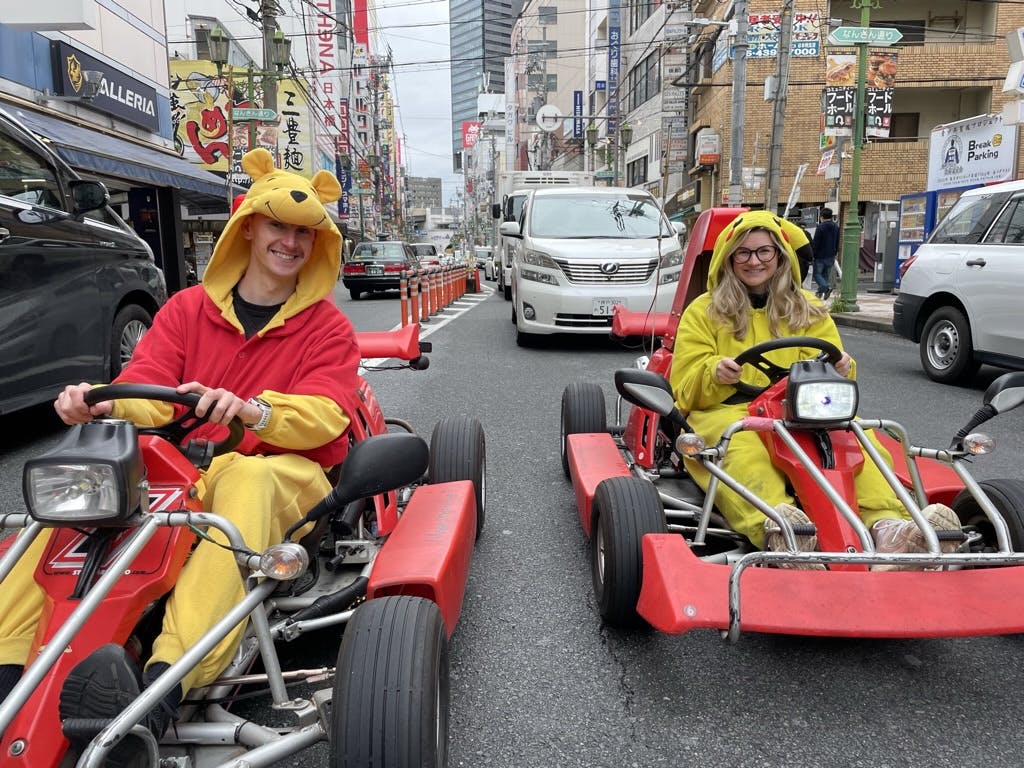 Two people in fancy dress sat in go-karts on an Osaka street